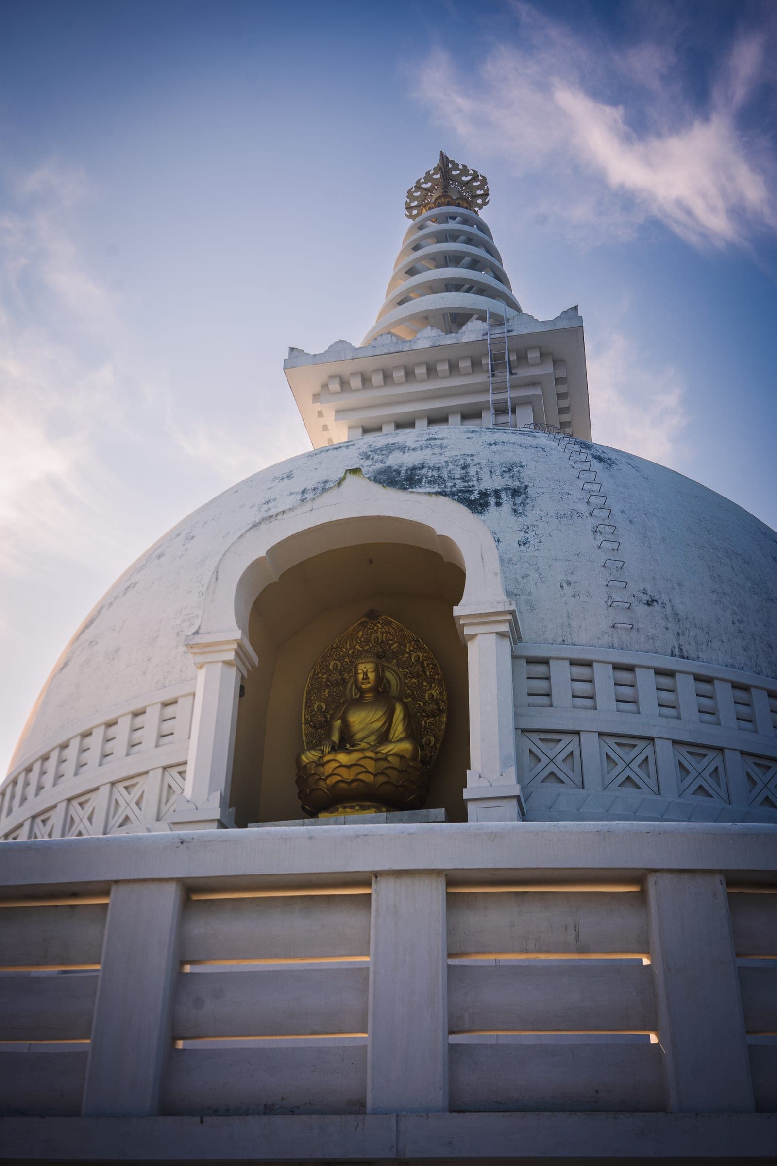A white peace pagoda with a golden Buddha alcove against a clear blue sky