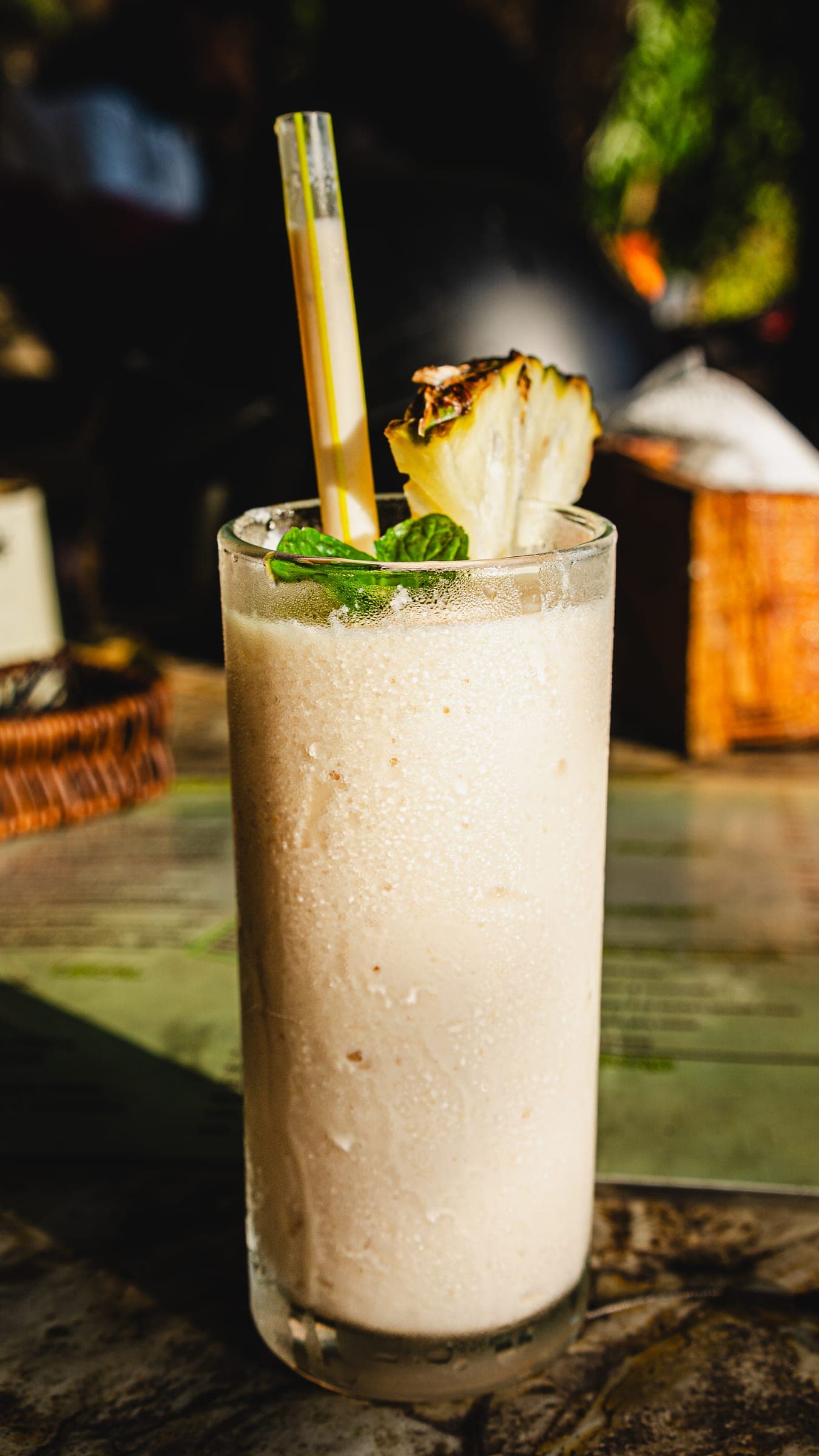 A tall glass of blended pineapple drink with mint and a grilled pineapple wedge
