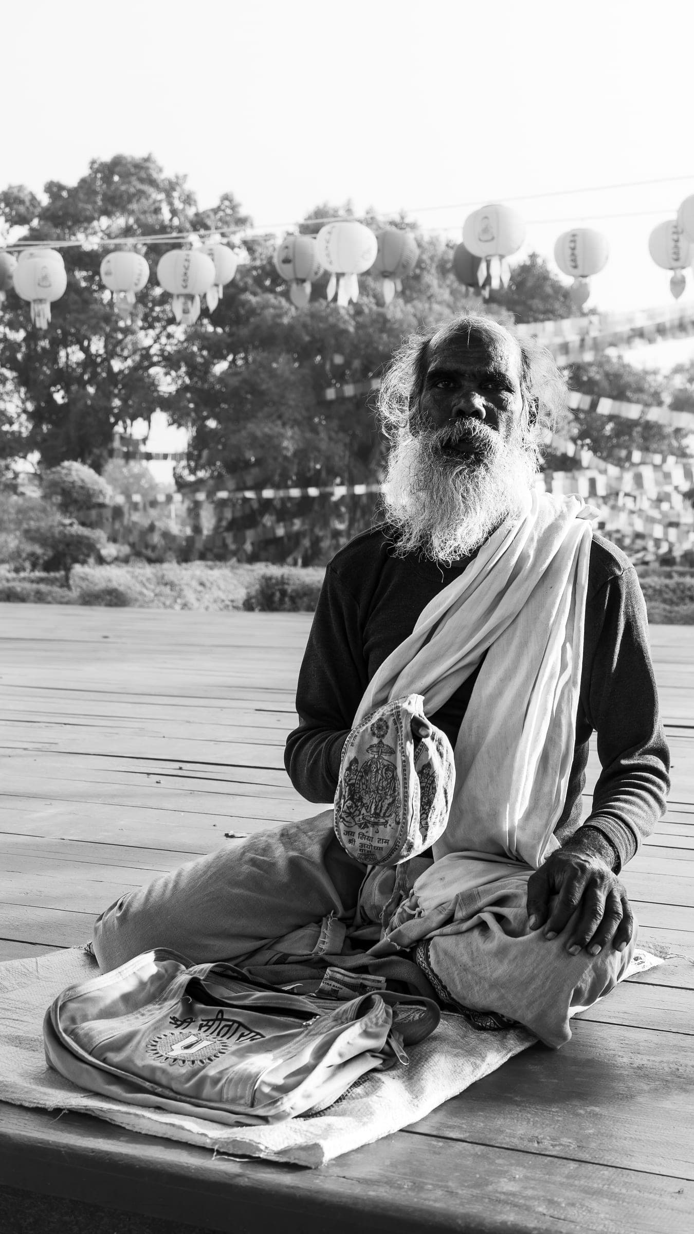 Black-and-white portrait of an elderly man with a long white beard sitting cross-legged outdoors