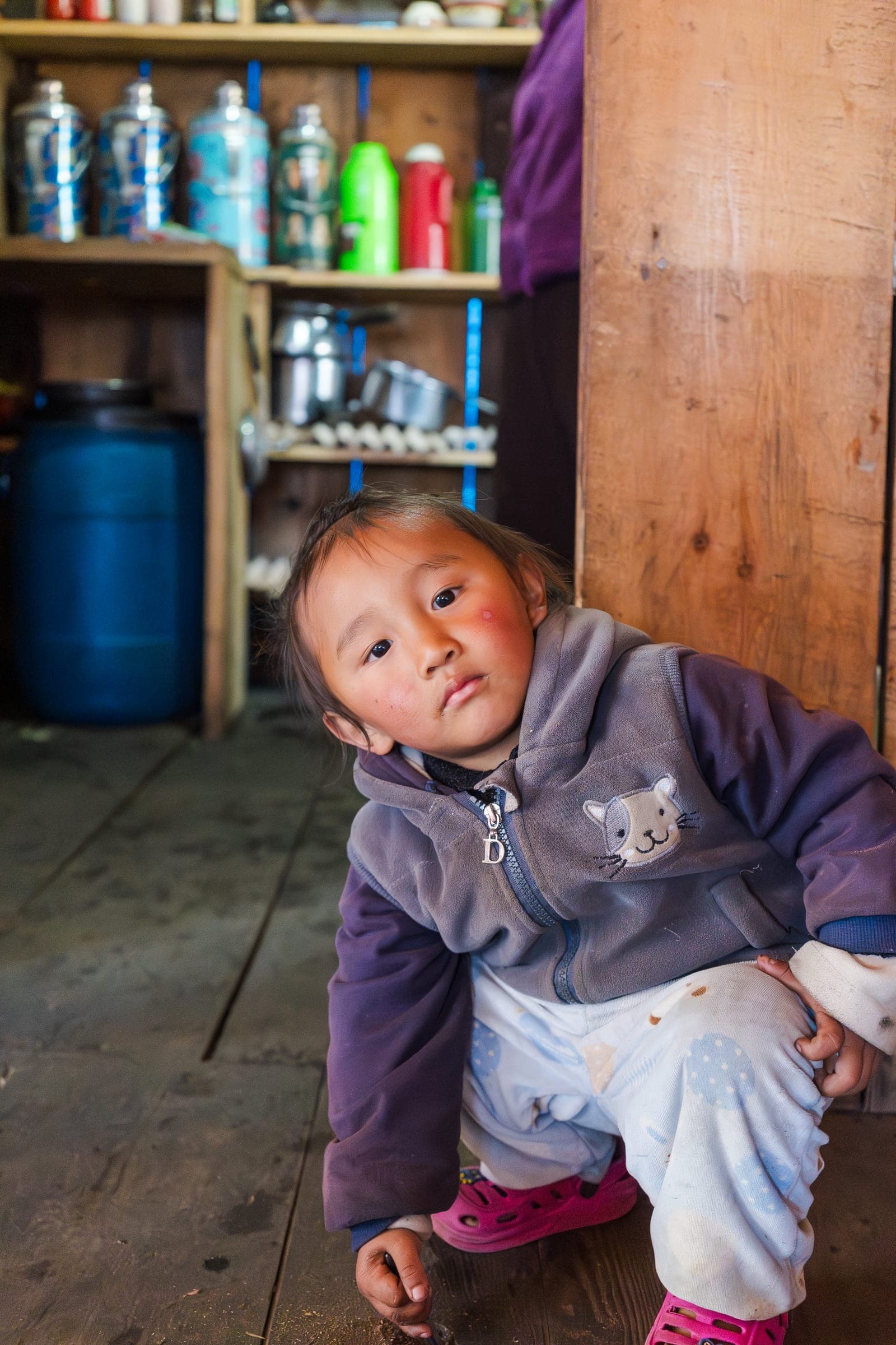 A child in a purple fleece crouching on a wooden lodge floor