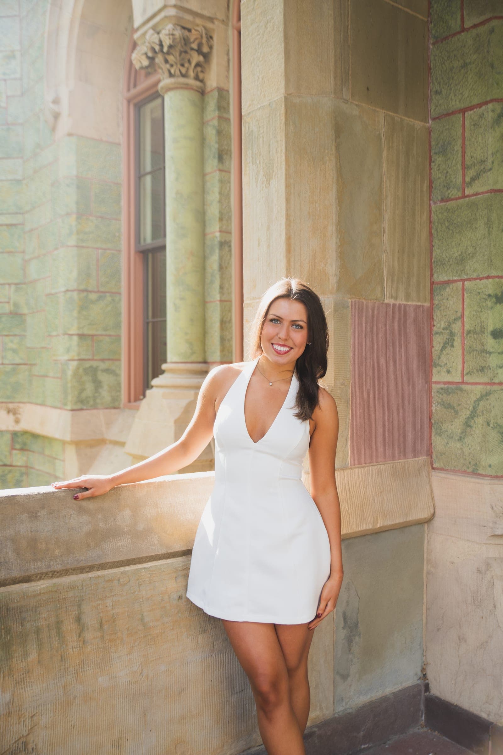 A young woman in a white halter dress leaning against stone campus architecture