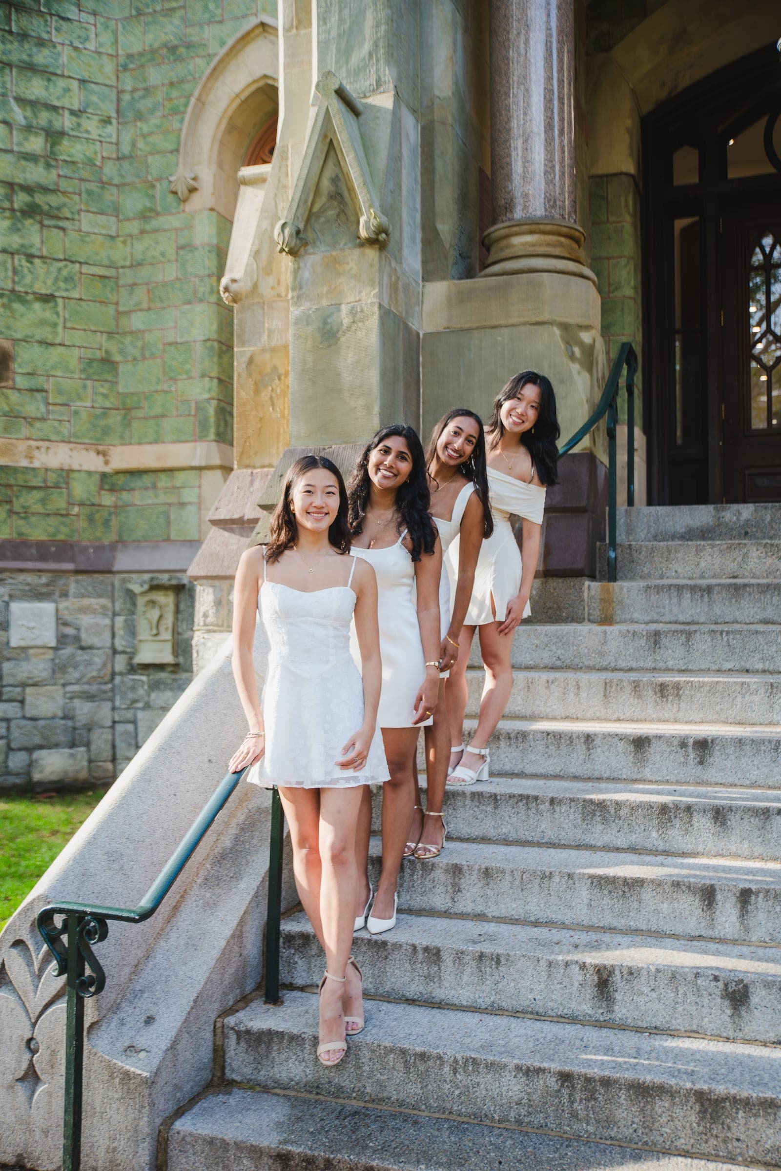 Four women in white dresses standing on the stone steps of a historic campus building